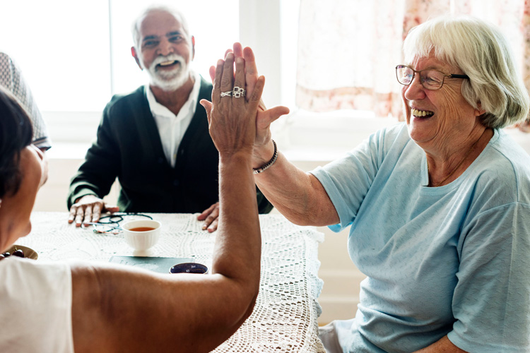 Dayspring Villa Assisted Living Community in Denver, CO - dayspring villa senior woman high fiving a friend at mealtime Dayspring Villa Assisted Living Community in Denver, CO - dayspring villa senior woman high fiving a friend at mealtime
